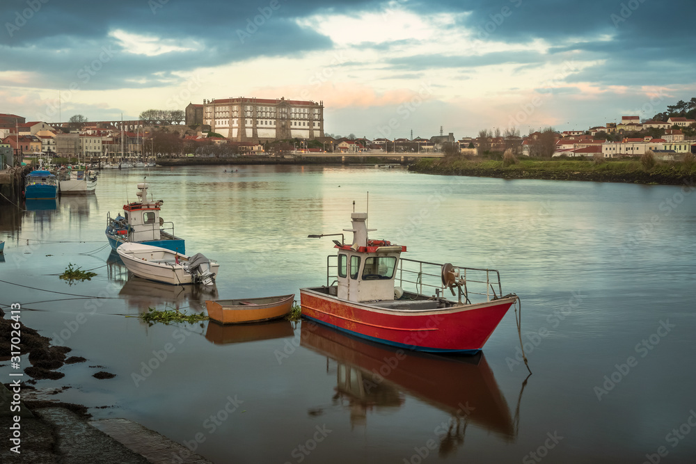 View of the Ave river in Vila do Conde, Portugal, with fishing boats anchored in the foreground and the Santa Clara convent in the background, at the end of an autumn day.