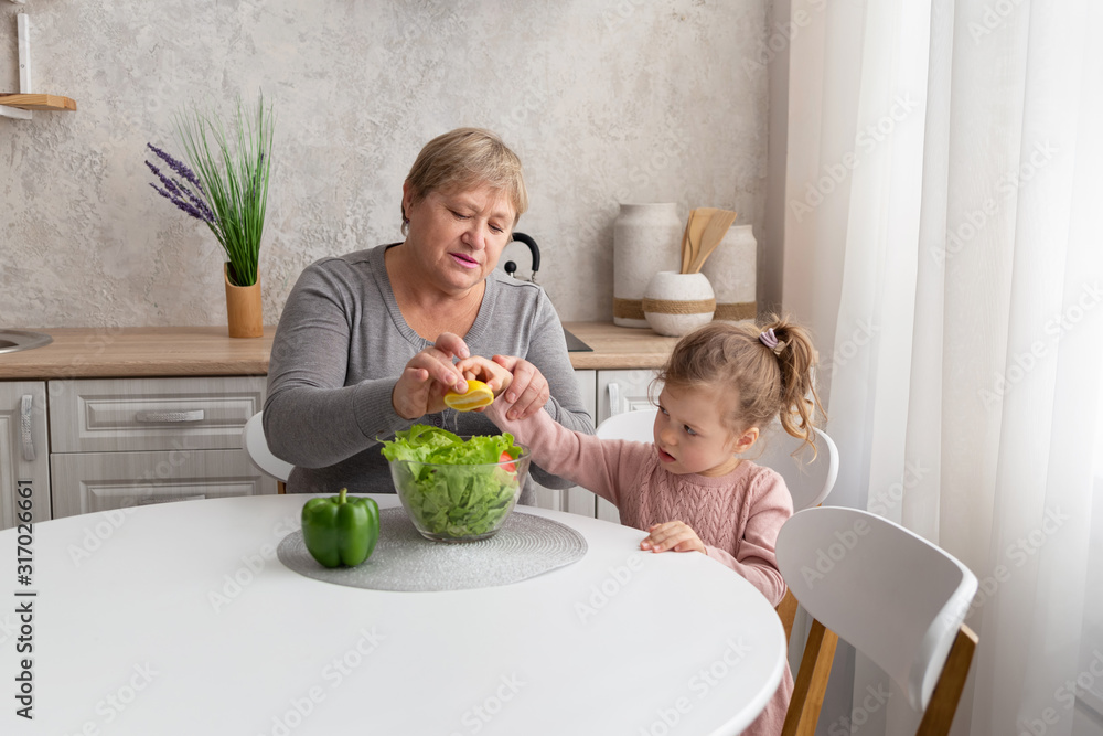 Happy grandmother and granddaughter prepare salad together in the light kitchen. Family cooking healthy food