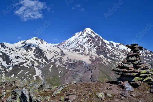 Beautiful impozant Kazbek mountain  covered with glacier, Georgia. Stone pyramid in the foreground. Sunny day, blue sky with white clouds. photo