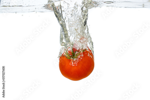 red tomato with a green tail drops under water on a white background