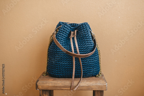 Trendy blue knitted hand bag, made from nylon thread, is on wooden chair. Handmade pattern. photo