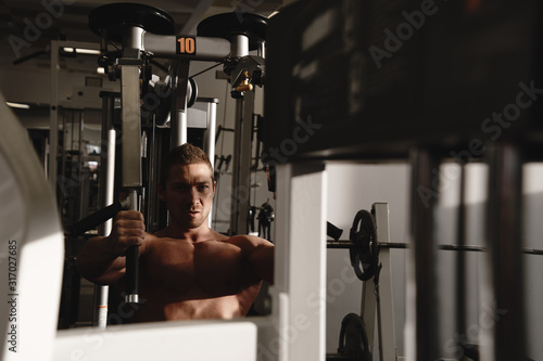 Portrait of fitness athlete man with muscular body does exercises on sports equipment in the gym, workout arm muscles, pumping biceps and triceps