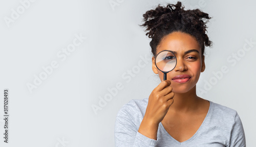 Curious girl holding magnifier over grey background