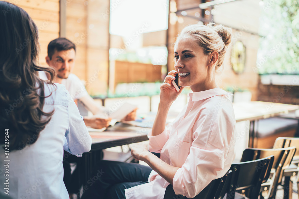 Pleased woman phoning while sitting with colleagues at table on terrace Pleased woman phoning while sitting with colleagues at table on terrace