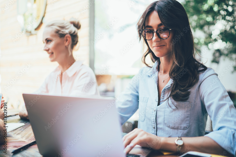 Pensive woman using laptop while sitting beside colleagues at table Pensive woman using laptop while sitting beside colleagues at table