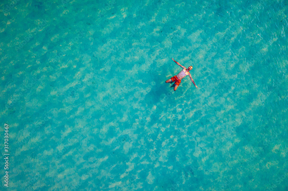 Drone view of a man floating in tropical sea water. Aerial view of young man floating on sea water enjoying sunbathing and vacations in tropical destination. People travel tourism holidays concept.