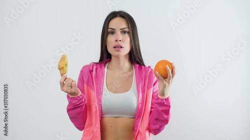 Fit woman in sportswear choosing between orange and croissant over white background. Diet concept. photo