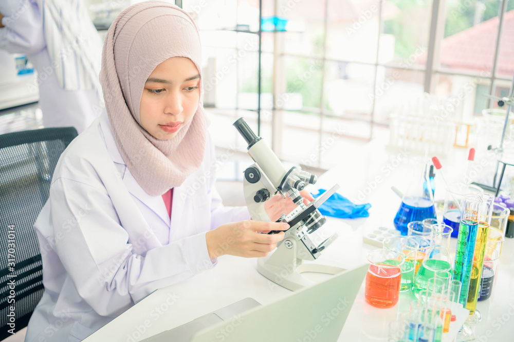 Fototapeta premium Lab worker. Positive muslim woman looking into the microscope while being at work in the lab