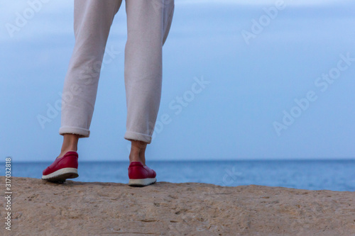 Young woman on Rock seaside. Stoned beach near sea with blue sky