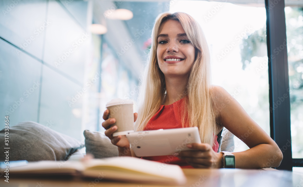 Fototapeta premium Cheerful woman with takeaway beverage and tablet in cafe