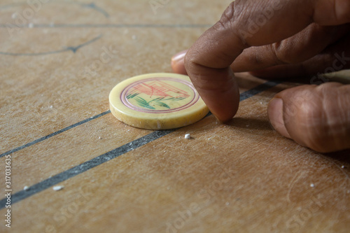 Person ready to strike the coins in carrom board game. Multiplayer board game with good fun time.