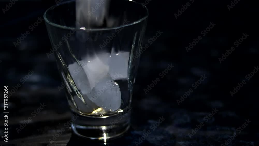 Ice is poured into a transparent glass on a dark background. Then brown soda water and lemonade are poured into the same place. Ice is poured into a transparent glass on a dark background. Then brown soda water and lemonade are poured into the same place.