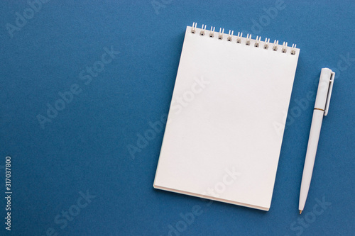 Blank notepad and pen on trendy dark blue background. Notebook for ideas message, list and inspiration. Top view, flat lay with copy space. Mockup for your design.  photo
