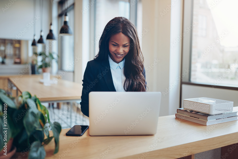 Smiling African American businesswoman using a laptop in an offi Smiling African American businesswoman using a laptop in an offi
