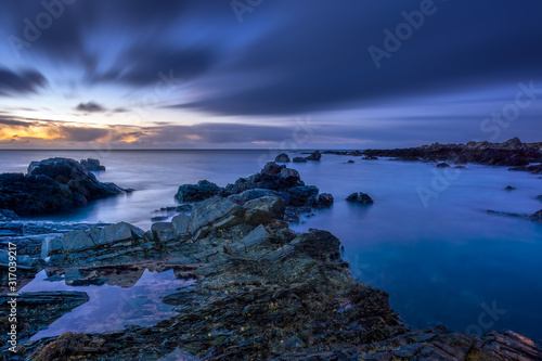 Twilight begins yielding to daylight at rocky coastline with blurred water and sky  long exposure photography. Northern Ireland