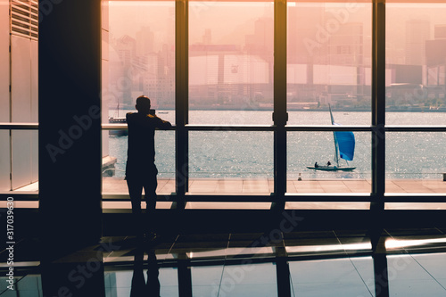 person looking on mobile phone at office window with sailboat in background