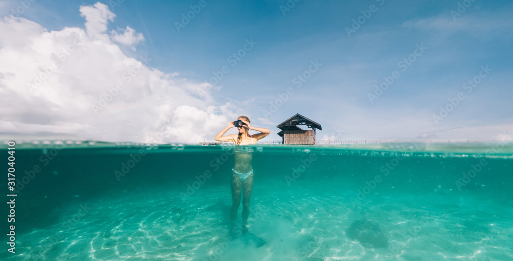 Carefree female submerged at oceania shallow happy from spending free time for Indonesian holidays, happy woman in snorkel mask enjoying recreation at waterline with touristic bungalow on background