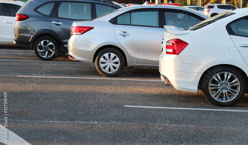 Closeup of rear, back side of white car with other cars parking in outdoor parking area in bright sunny day..