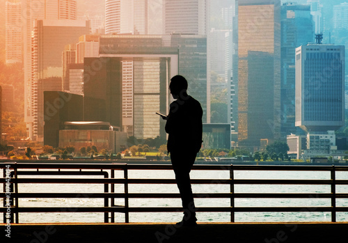 Fotografie Silhouette of a man looking on mobile phone with Hong Kong Island city skyline b
