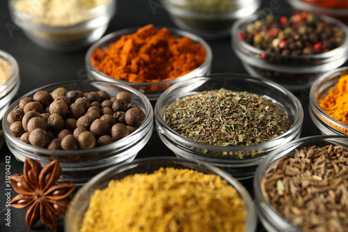 Bowls with different spices and ingredients on black background, close up