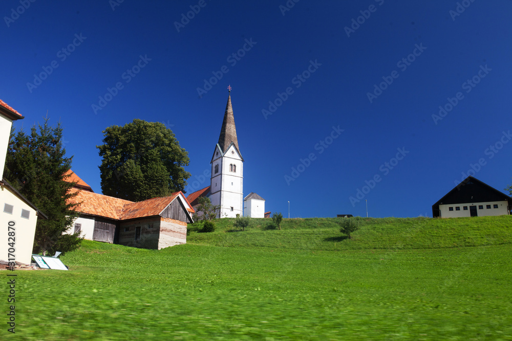Little white  church in Slovenian countryside among lush green summer landscape and blue sky