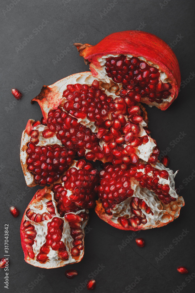 The opened Fruits of a ripe open pomegranate lie on a black textural background.