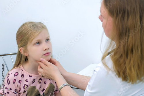 Medicine for children and healthcare concept. Pediatrician woman probing touching lymph nodes on neck of girl child during preventive examination. Doctor diagnostics tonsillitis or angina.