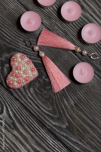 Earrings tassels pink. Brooch made of beads. Near decorative candles. On brushed pine boards painted in black and white.