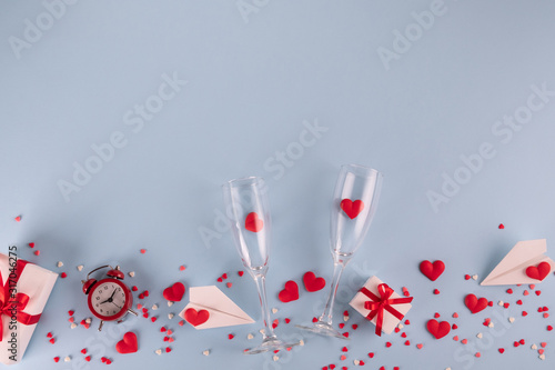 Valentine's Day background. Gift box , alarm clock , red candy  hearts and paper plane, two champagne glasses on pastel blue background. Valentines day concept. Flat lay, top view, copy space