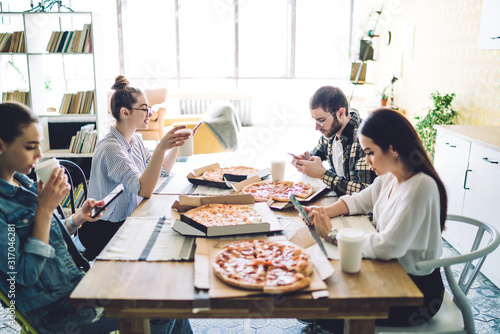 Woman drinking coffee and surfing smartphone with friends at table with pizza