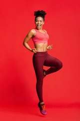 Cheerful fitness girl exercising over red background
