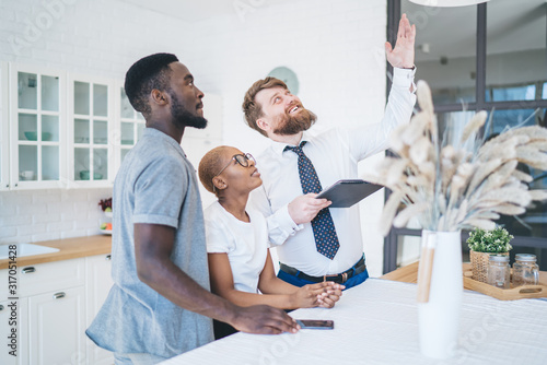 Tapeta Serious ethnic couple and real estate agent inspecting ceiling in new apartment