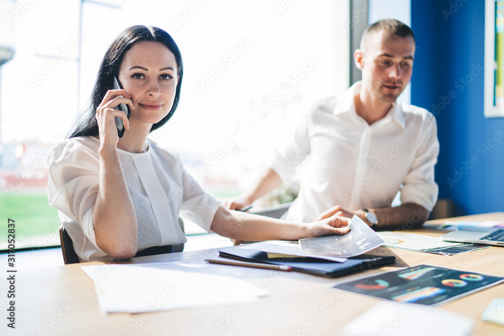 Smiling elegant businesswoman phoning while sitting at table in office Smiling elegant businesswoman phoning while sitting at table in office