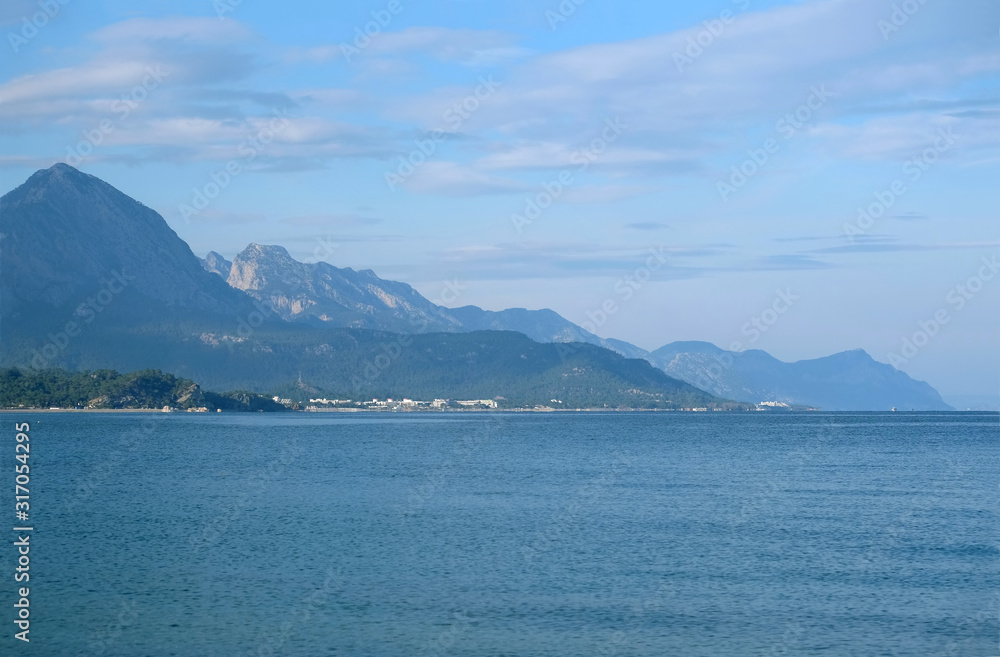 Beautiful landscape with calm sea, coastline, and high mountains covered with green forests