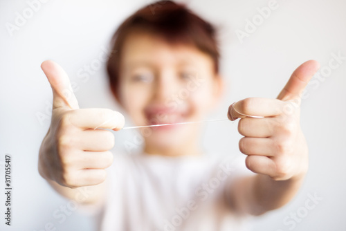 Closeup of dental floss in child hands. Happy child in white t-shirt out of focus hold floss for teeth in two hands. Dental and health care. Correct dental care from childhood save teeth for life.