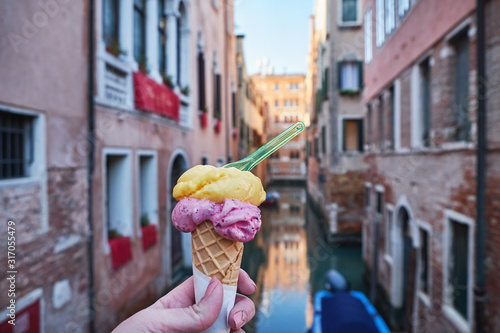 Woman hand holding italian gelato ice cream cone on the bridge in Venice, Italy. Sunny day, historical buildings and the canal in the background. Close up. Travel concept.
