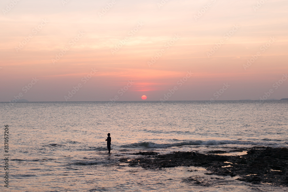 Fisherman in the hat on sea pink sunset background.
