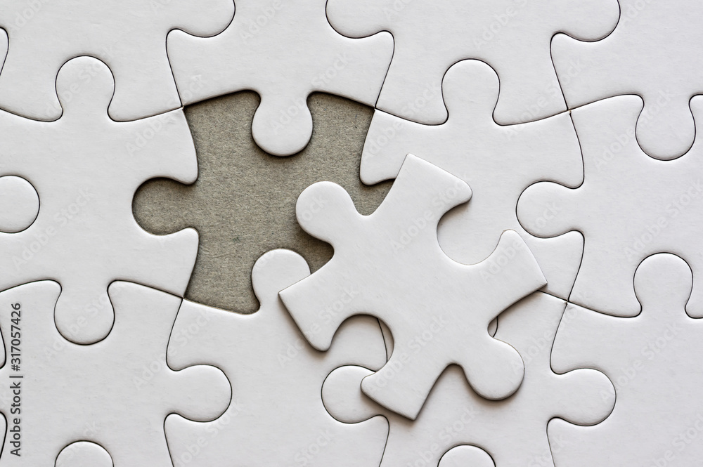 Close up on blank, white jigsaw puzzle pieces. One piece is removed, to the side Close up on blank, white jigsaw puzzle pieces. One piece is removed, to the side
