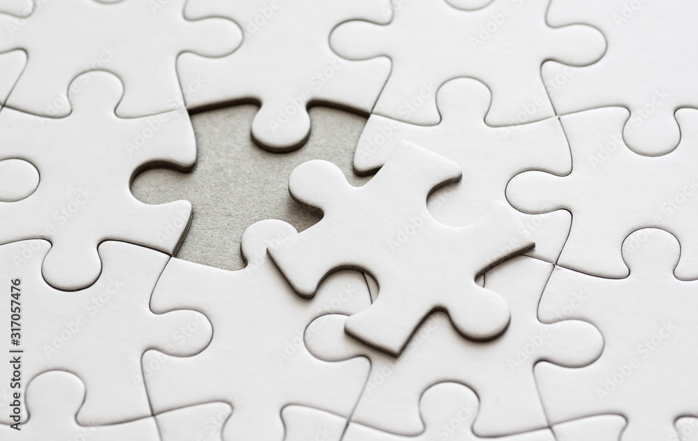Close up on blank, white jigsaw puzzle pieces. One piece is removed, to the side Close up on blank, white jigsaw puzzle pieces. One piece is removed, to the side