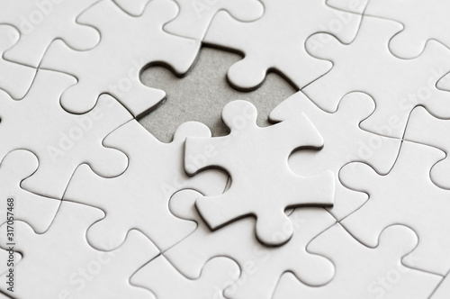 Close up on blank, white jigsaw puzzle pieces. One piece is removed, to the side
