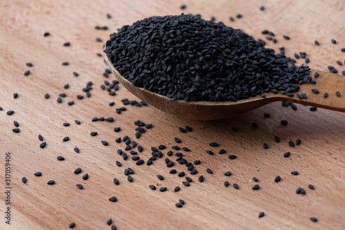 Full spoon of black sesame seed on a wooden board. Wooden spoon on a white background. Home cooking.