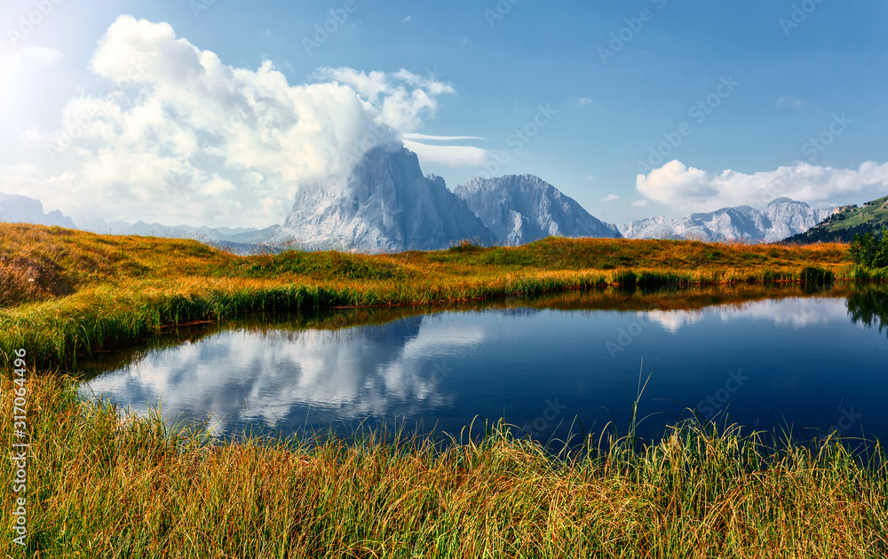 Incredible Nature landscape of Dolomites Alps in spring time. Wonderful Mountain valley with fresh green grass, clear lake and majestic Sassolungo peak. Perfect countryside scenery in sunny day.