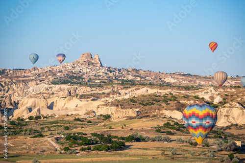 Cappadocia, Turkey: aerial view of Uchisar, ancient town of the historical region in Central Anatolia rich of exceptional natural wonders, with hot air balloons floating in the sky after dawn