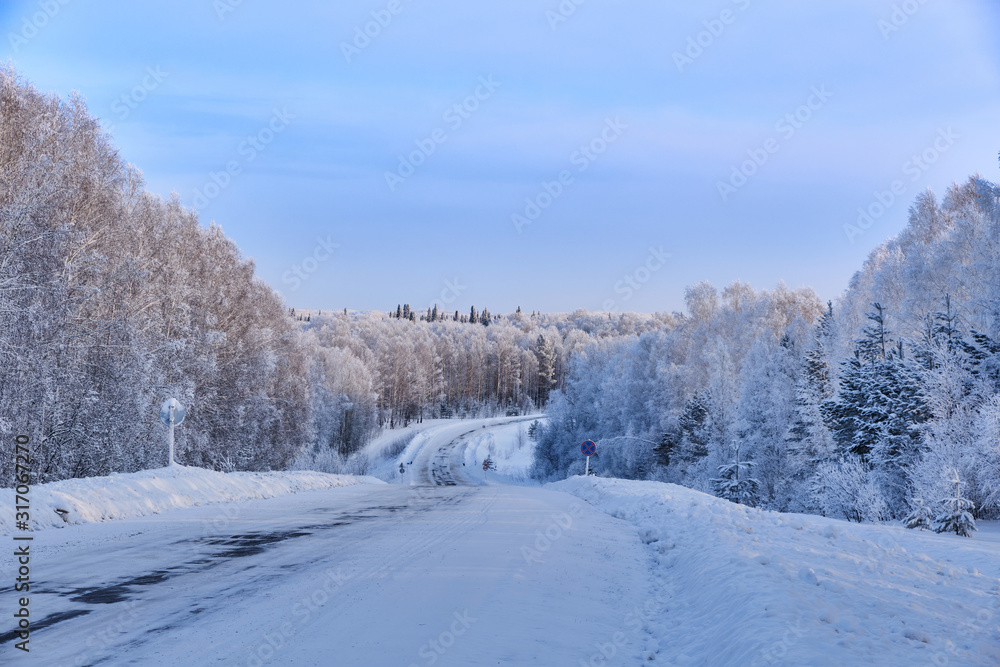 Winter landscape. Winding road through the snowy taiga. Along the edges of the pine, fir and birch are covered with snow. Western Siberia. Salair Ridge. Russia. Winter landscape. Winding road through the snowy taiga. Along the edges of the pine, fir and birch are covered with snow. Western Siberia. Salair Ridge. Russia.