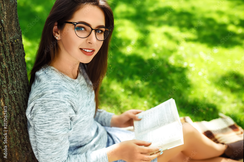 Beautiful girl in eyeglasses reading book in the summer park. Young student girl lies on green grass and reads a book. Concept of leisure and hobbies. Beautiful girl in eyeglasses reading book in the summer park. Young student girl lies on green grass and reads a book. Concept of leisure and hobbies.