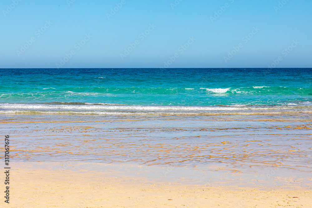 The beach in front and the sea with blue azure aquamarine turquoise colors in the background blue sky