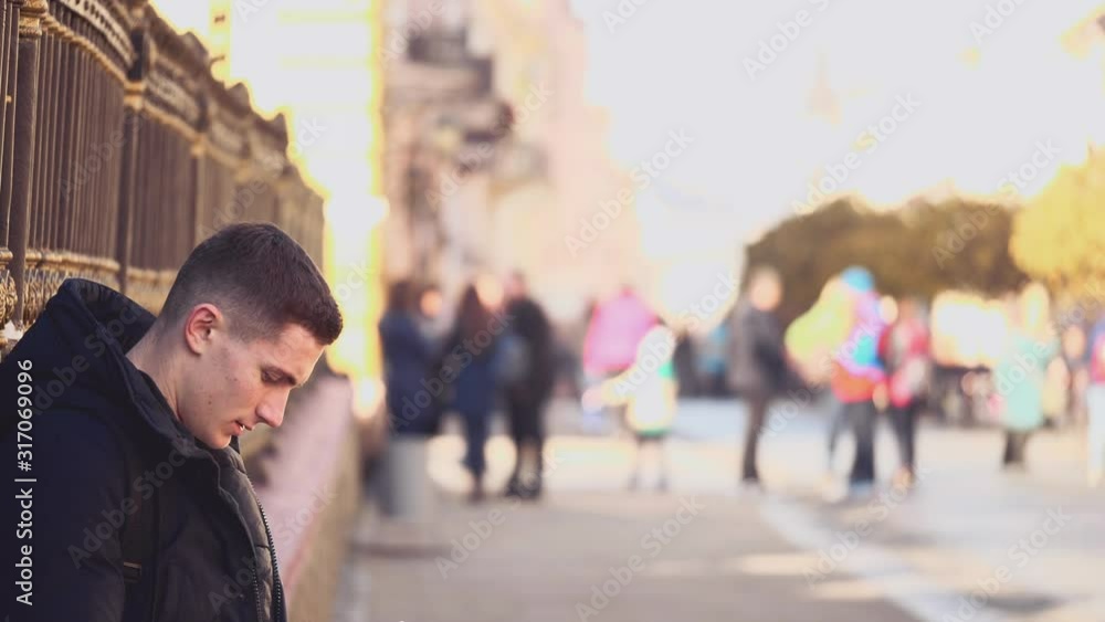 Handsome, attractive young man is going to sit on the fence. He is using his phone. Close up. Blurred background. Action. Animation. 4K. Handsome, attractive young man is going to sit on the fence. He is using his phone. Close up. Blurred background. Action. Animation. 4K.