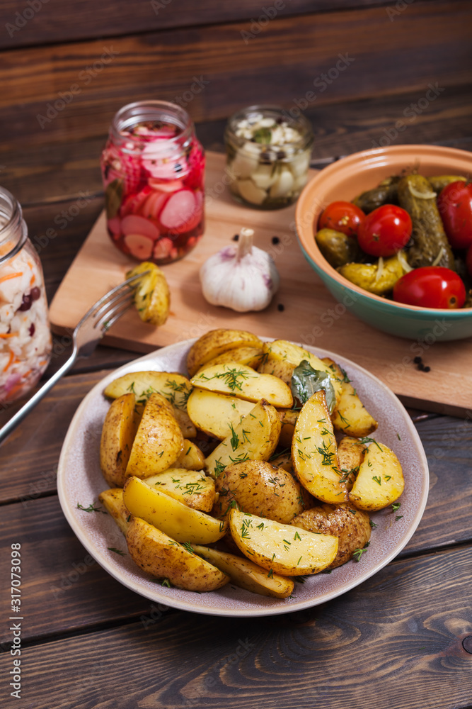 Potato slices baked in the oven with spices on a dark wooden background with pickles Potato slices baked in the oven with spices on a dark wooden background with pickles