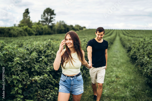 A tender loving couple walking in a field of currant. A smiling woman with long hair leads a man, holding his hand