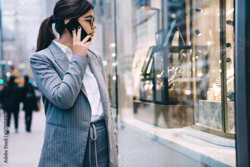 Confident formal young beautiful business lady talking on smartphone while walking on street